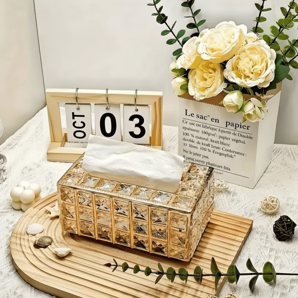 Porta-lenços dourado com cristais facetados e lenço saindo, com rosas e calendário ao fundo